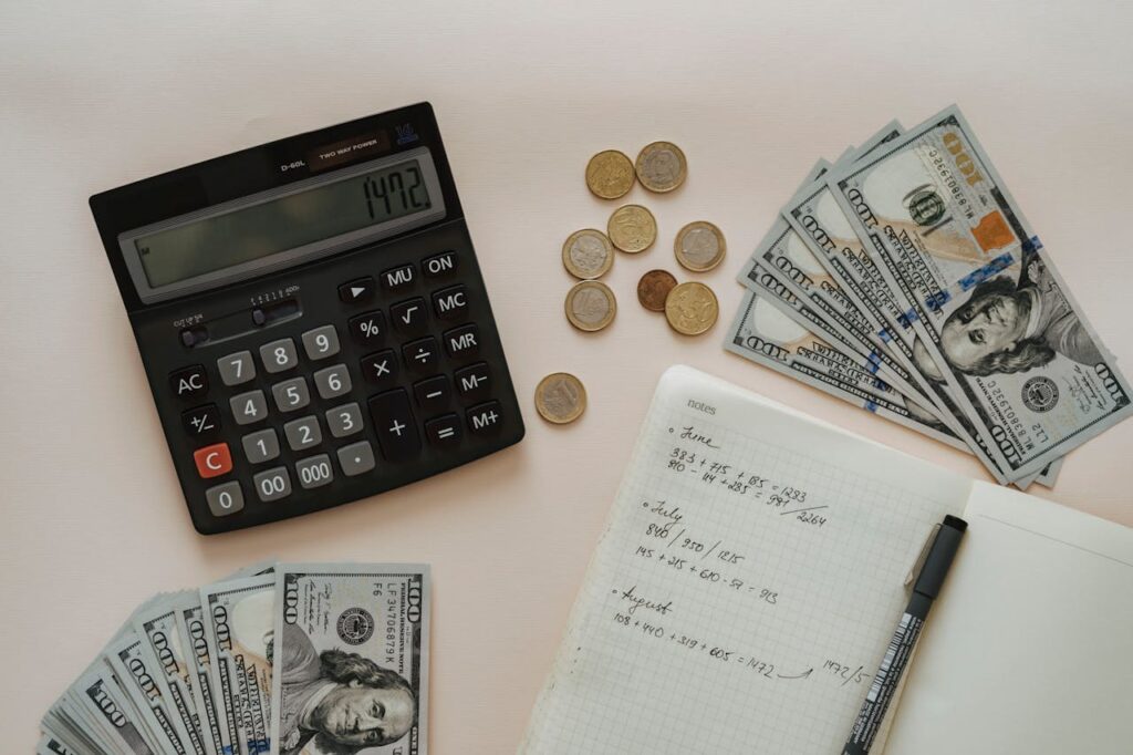 A black calculator beside coins and a notebook on a wooden surface, representing financial planning and budgeting challenges faced by landlords due to a nationwide rent cap.