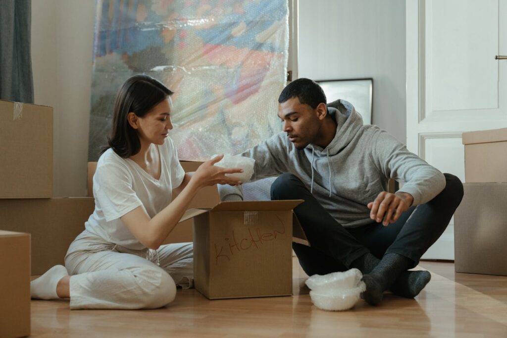 Man and woman packing boxes on their home's floor, preparing to sell a house as-is in Texas, showcasing the moving process.